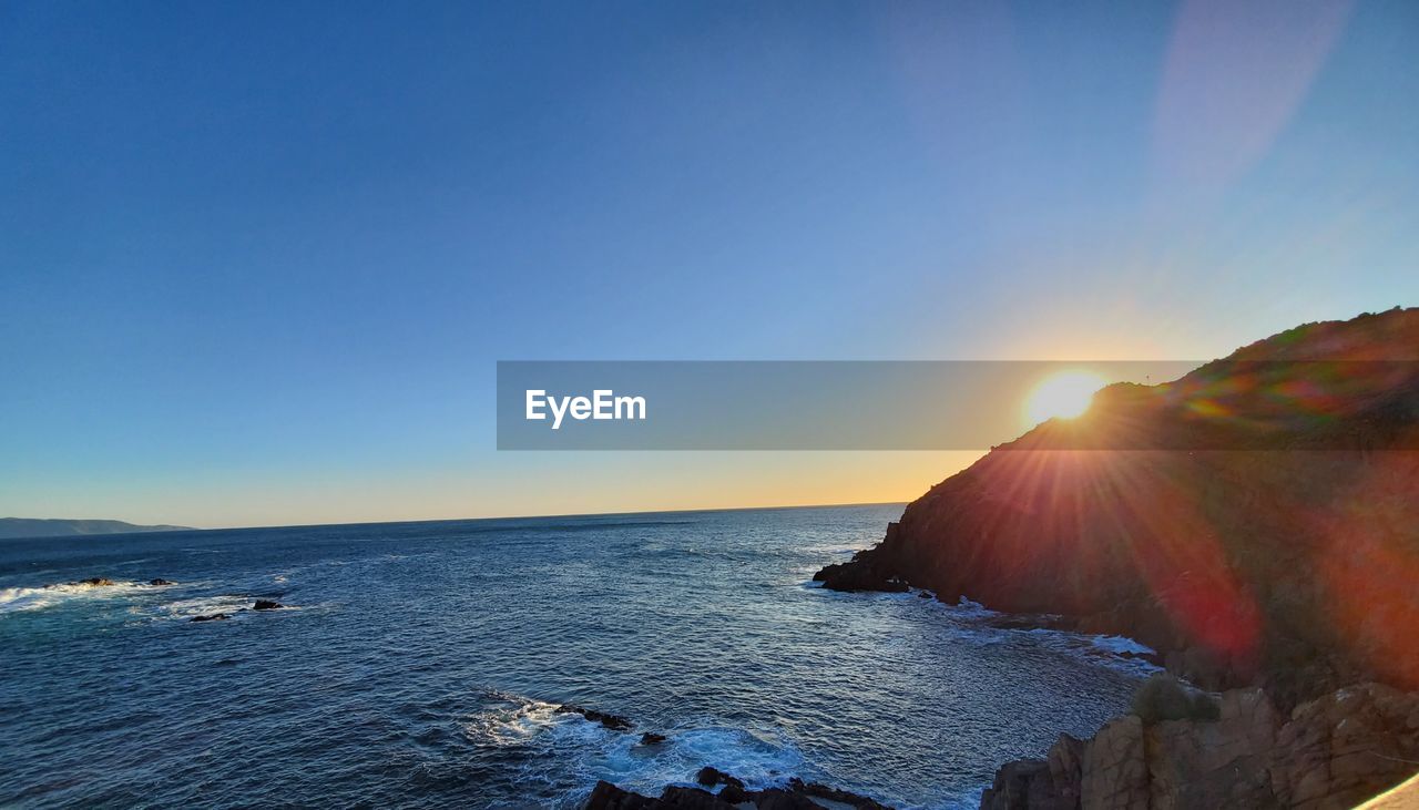 SCENIC VIEW OF SEA AGAINST BRIGHT SUN AT SUNSET