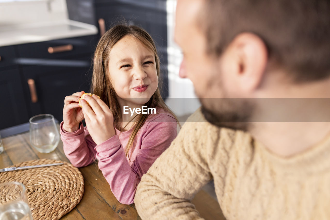 Smiling girl having breakfast with father sitting at table