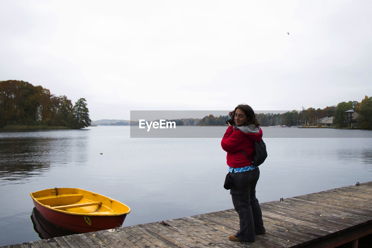 Woman standing on pier over lake against sky