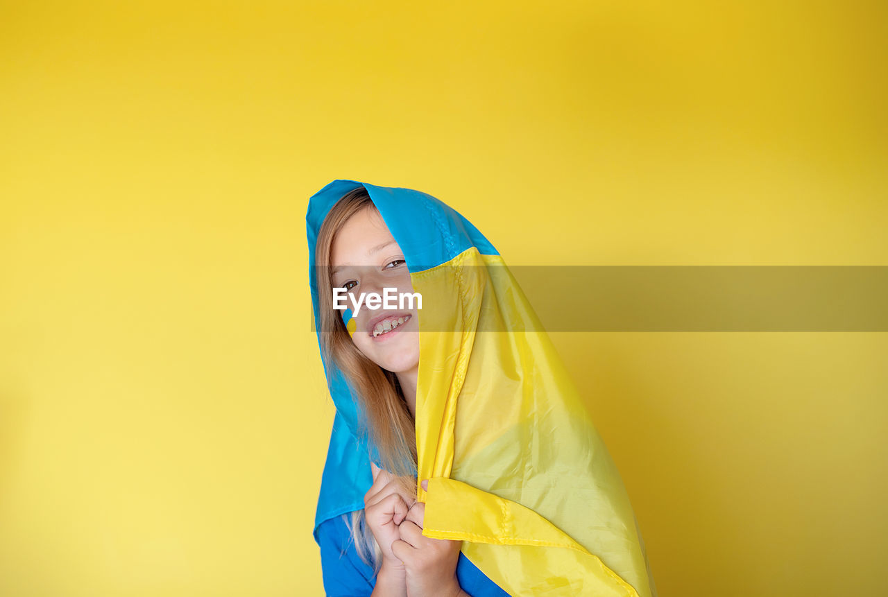 Portrait of young woman holding gift against yellow background