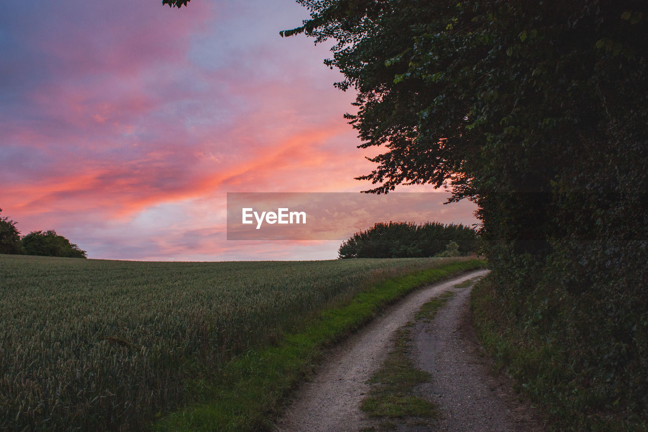 Road amidst field against sky during sunset