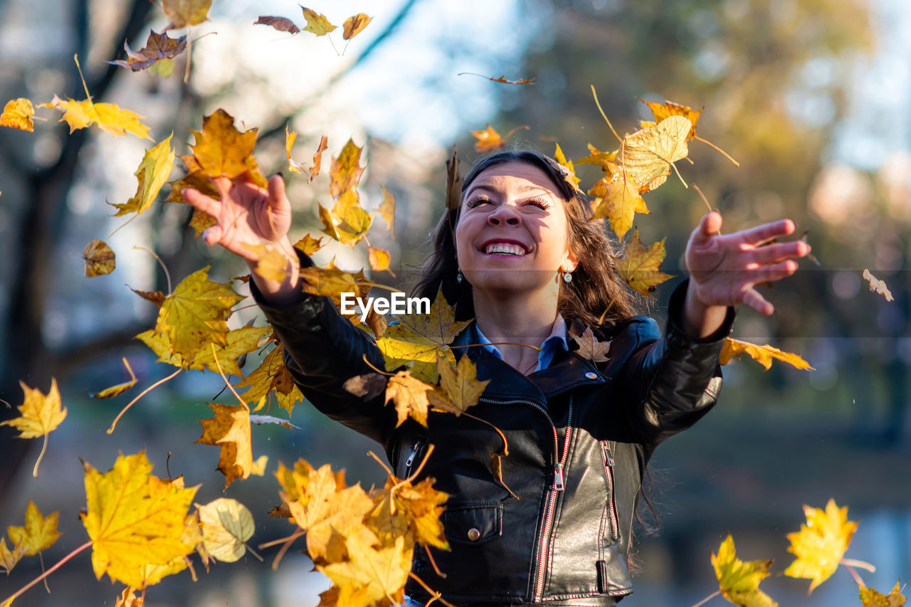Smiling young woman throwing maple leaf outdoors