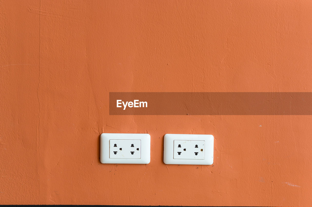 wall - building feature, electricity, power plugs and sockets, no people, white, orange color, copy space, indoors, orange, light switch, power supply, close-up, technology, wall, red