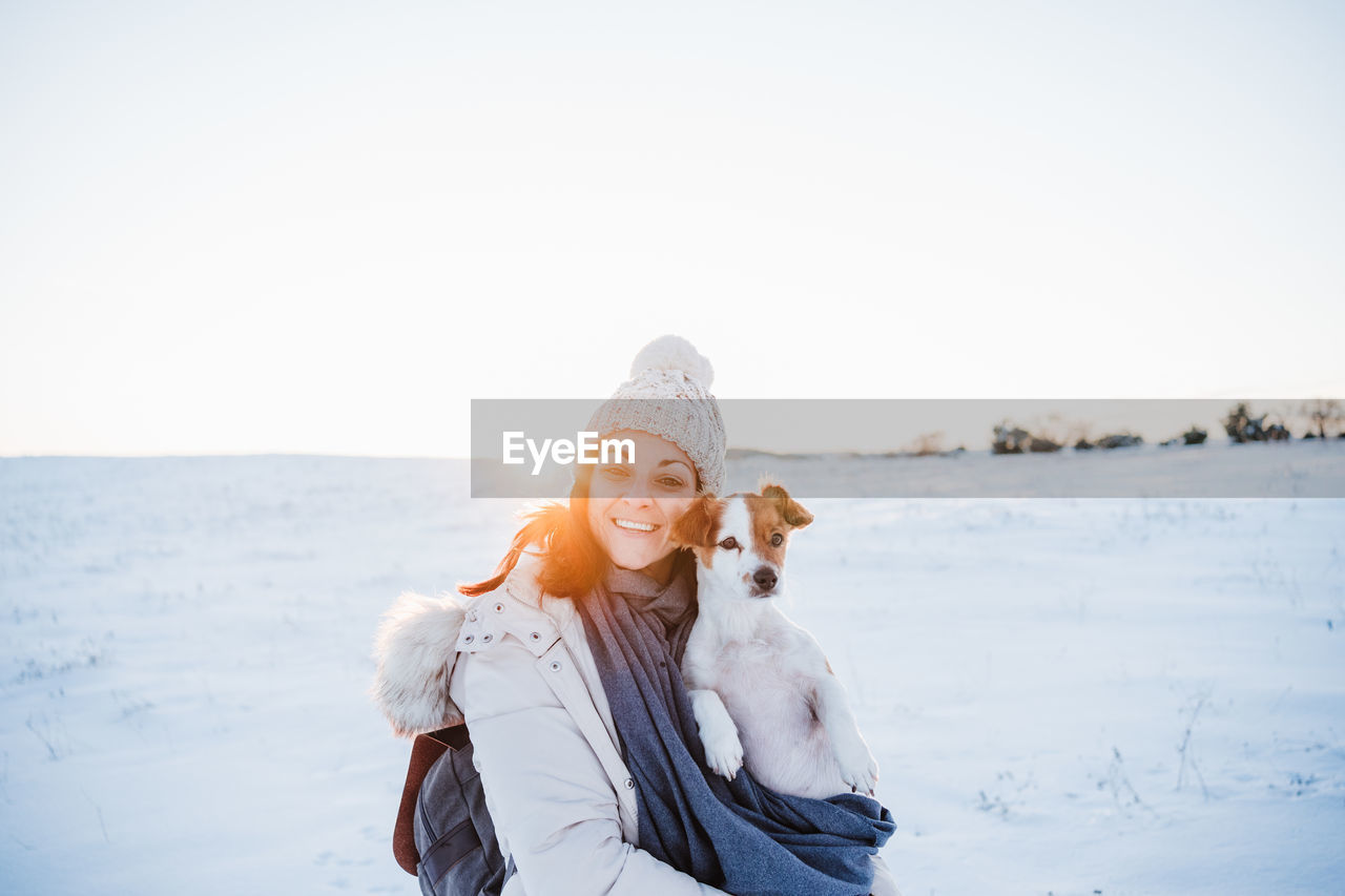 Portrait of smiling woman with dog on snow covered land against sky