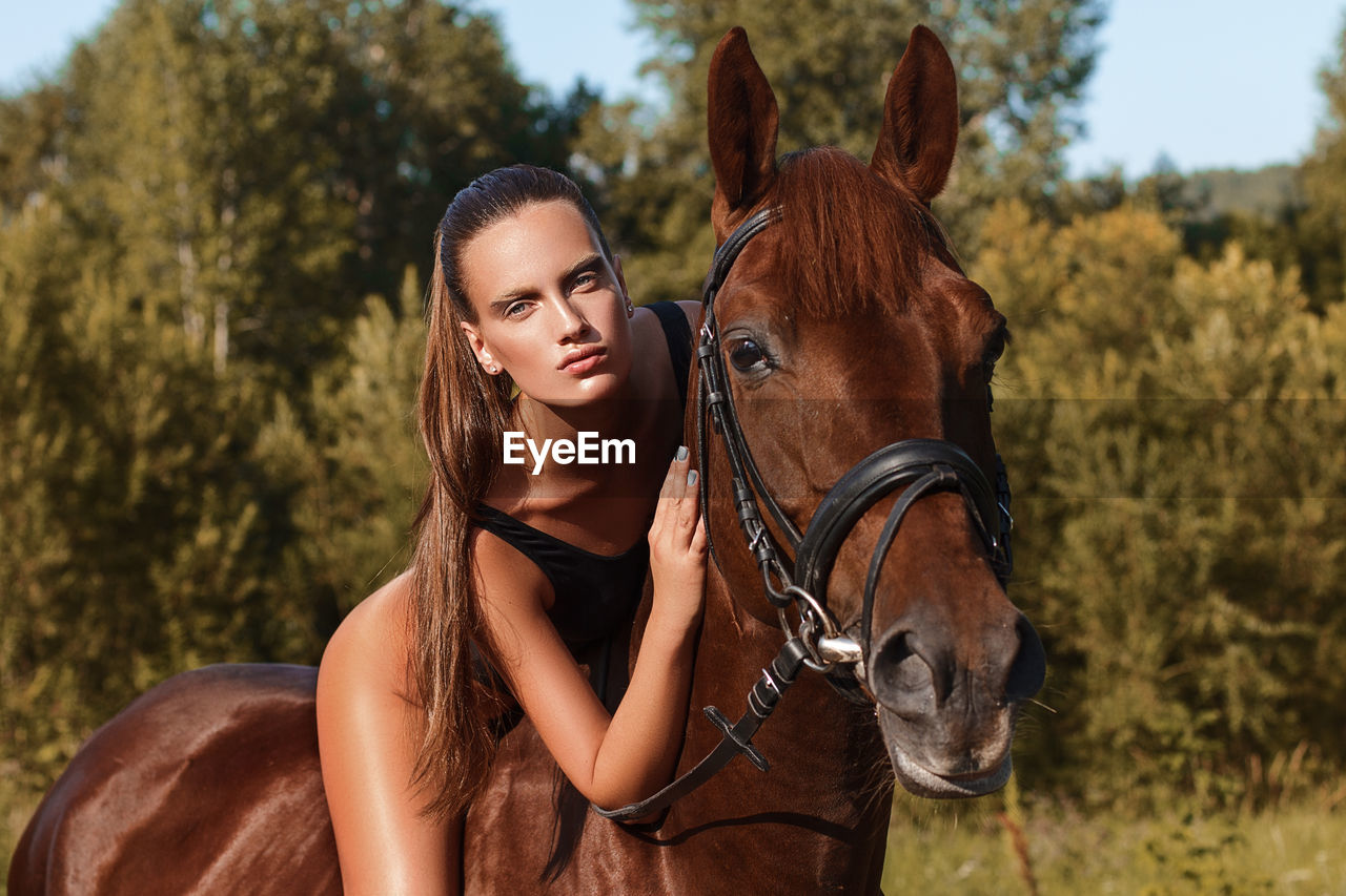 Portrait of seductive woman riding brown horse on field