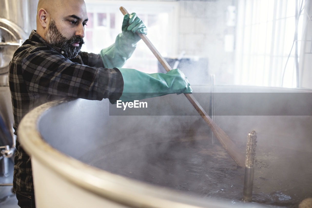 Mid adult worker stirring beer in container while working at brewery