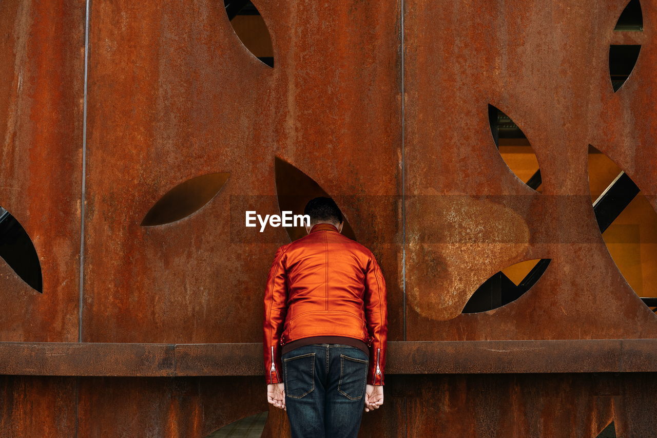 Rear view of man standing against orange rusty wall