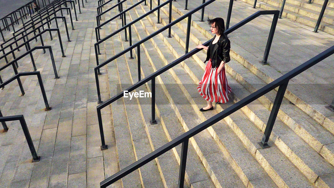 Full length of woman wearing striped skirt and jacket on steps amidst railing in city