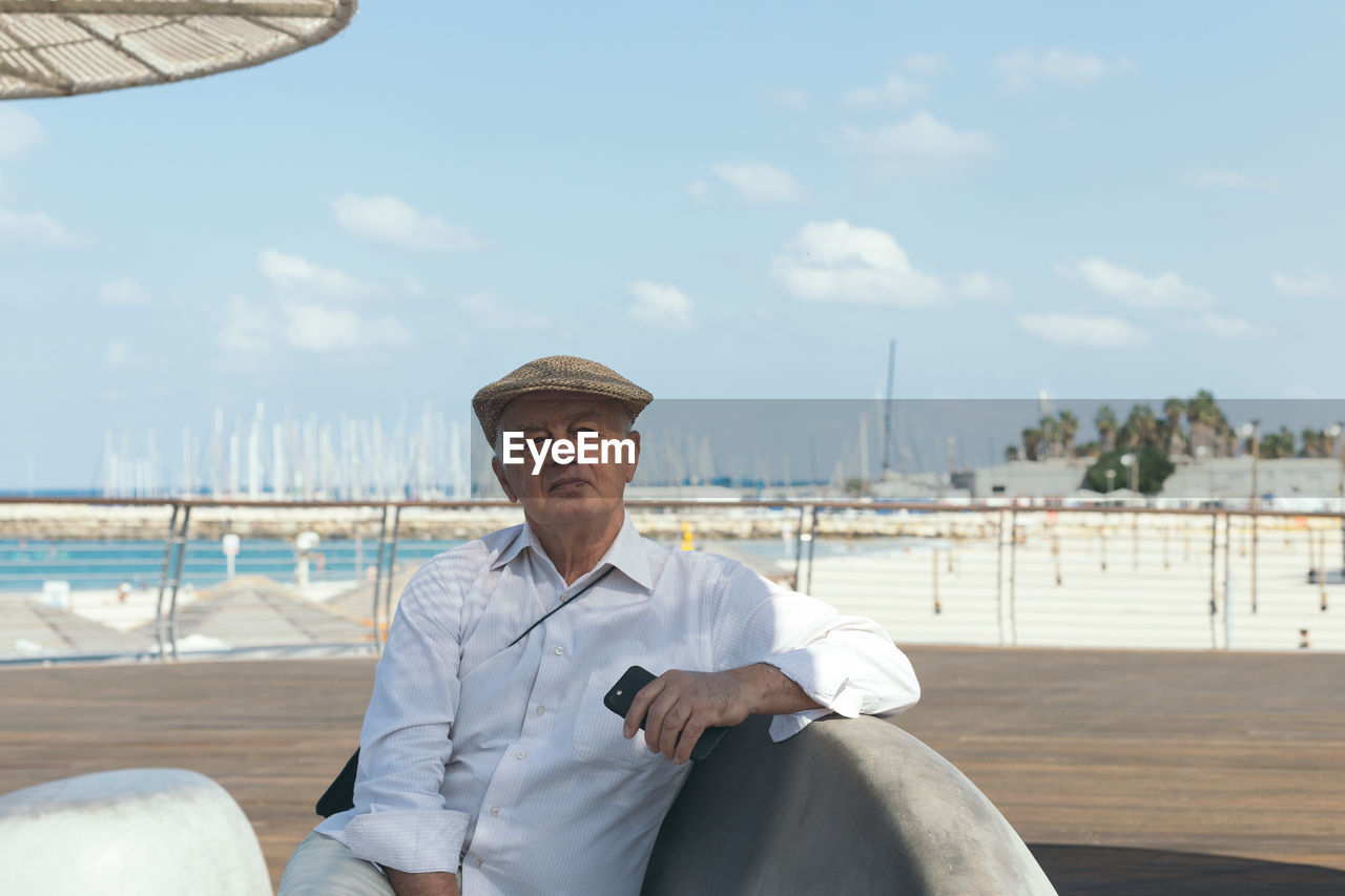 Portrait of senior man sitting on chair at harbor