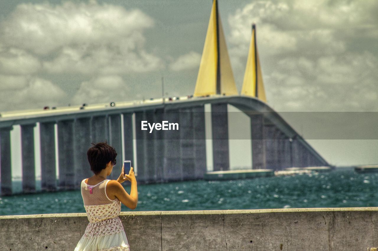 Rear view of woman photographing bridge in city