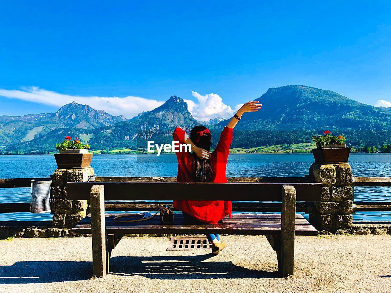 Rear view of woman sitting on bench by river against mountains
