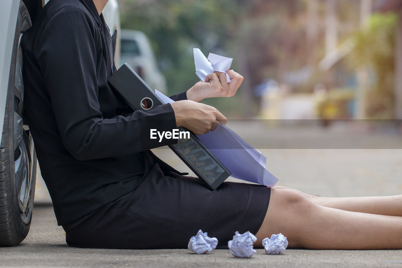 Midsection of businesswoman holding paper while sitting against car on street