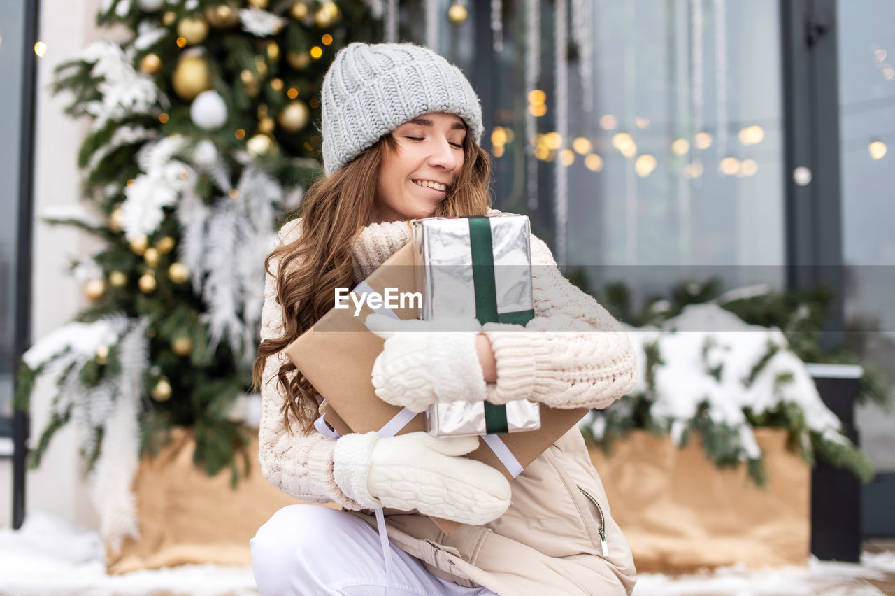 A cute girl in mittens has closed her eyes and is enjoying gifts on the street in winter in the city