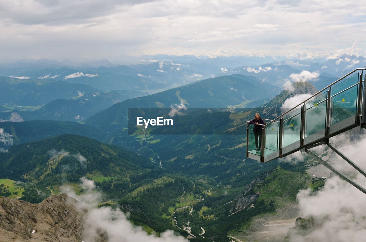 High angle portrait of woman standing on overhead cable car over mountains