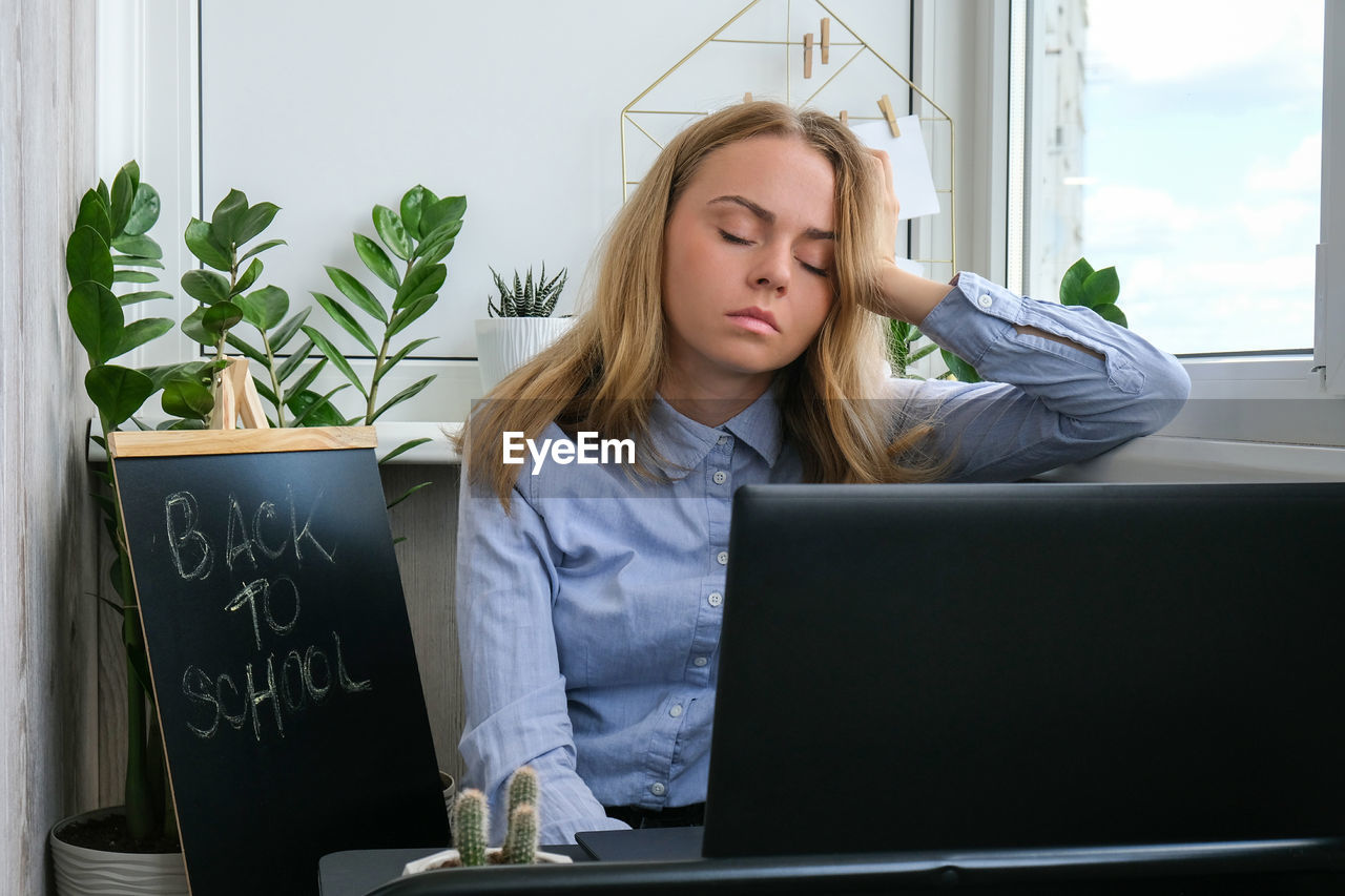 Tired sleepy young caucasian woman worker at desk workplace. overworking and sleeping deprivation. 