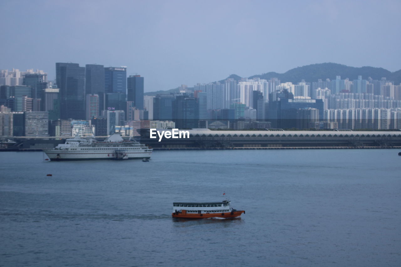 Boats in sea by buildings at city against clear sky