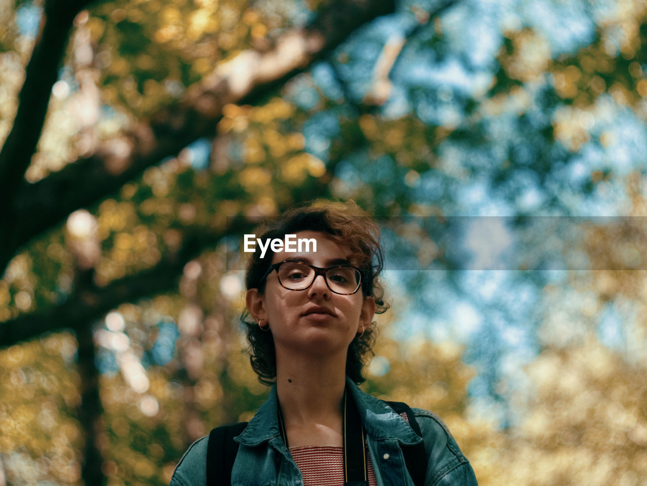 Low angle portrait of young woman standing against trees