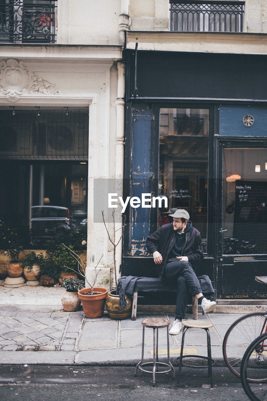 MAN SITTING ON CHAIR IN CITY AGAINST BUILDINGS