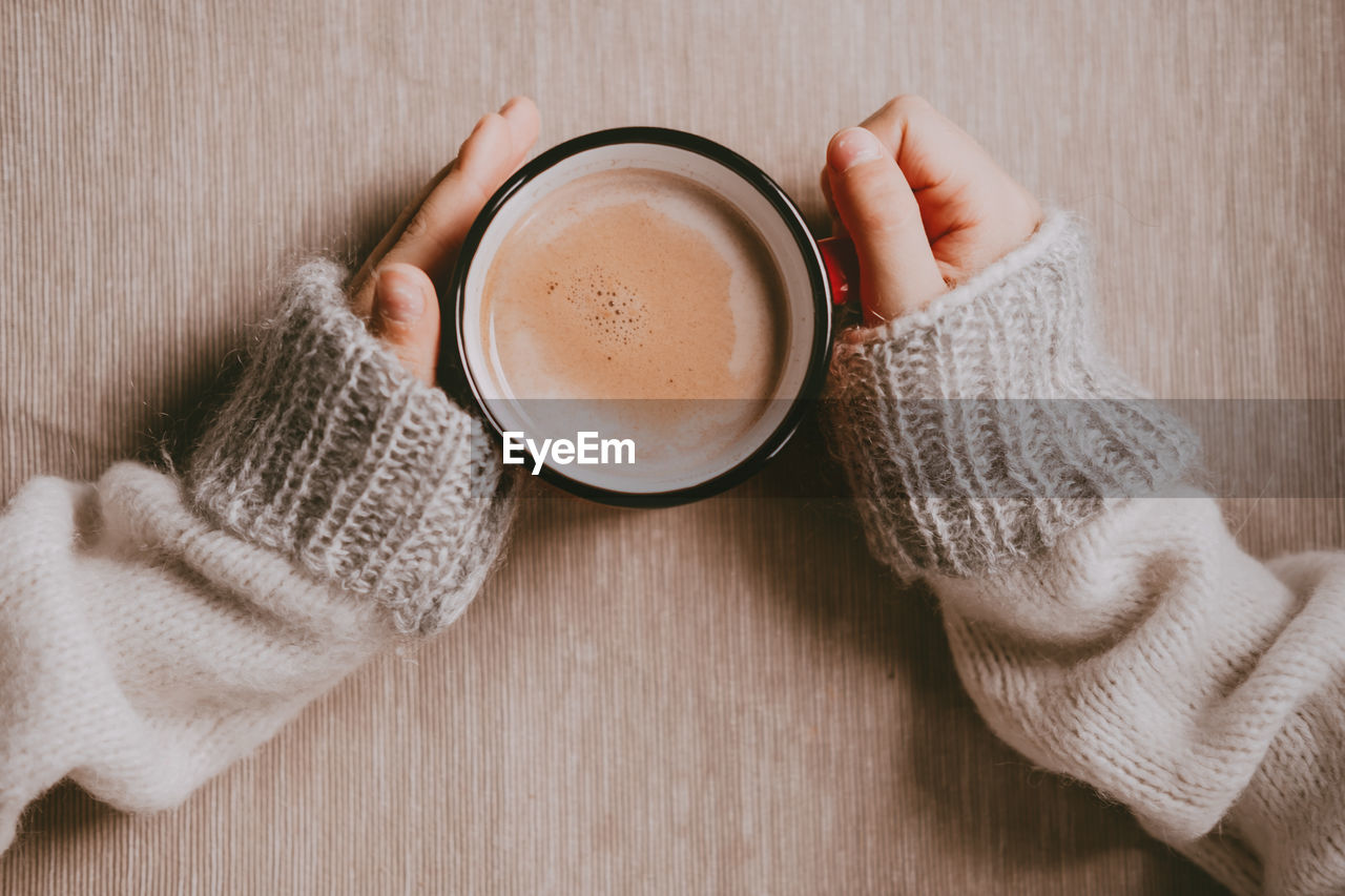 Hands in a sweater hold hot cocoa, in a red mug, top view. a cozy photo with a mug in hand