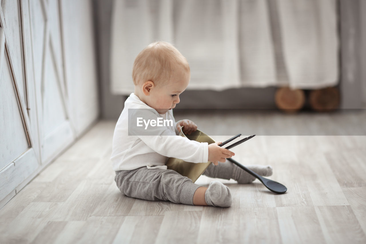 The blond kid plays with the kitchen tools on the floor, the concept of childhood and safety.