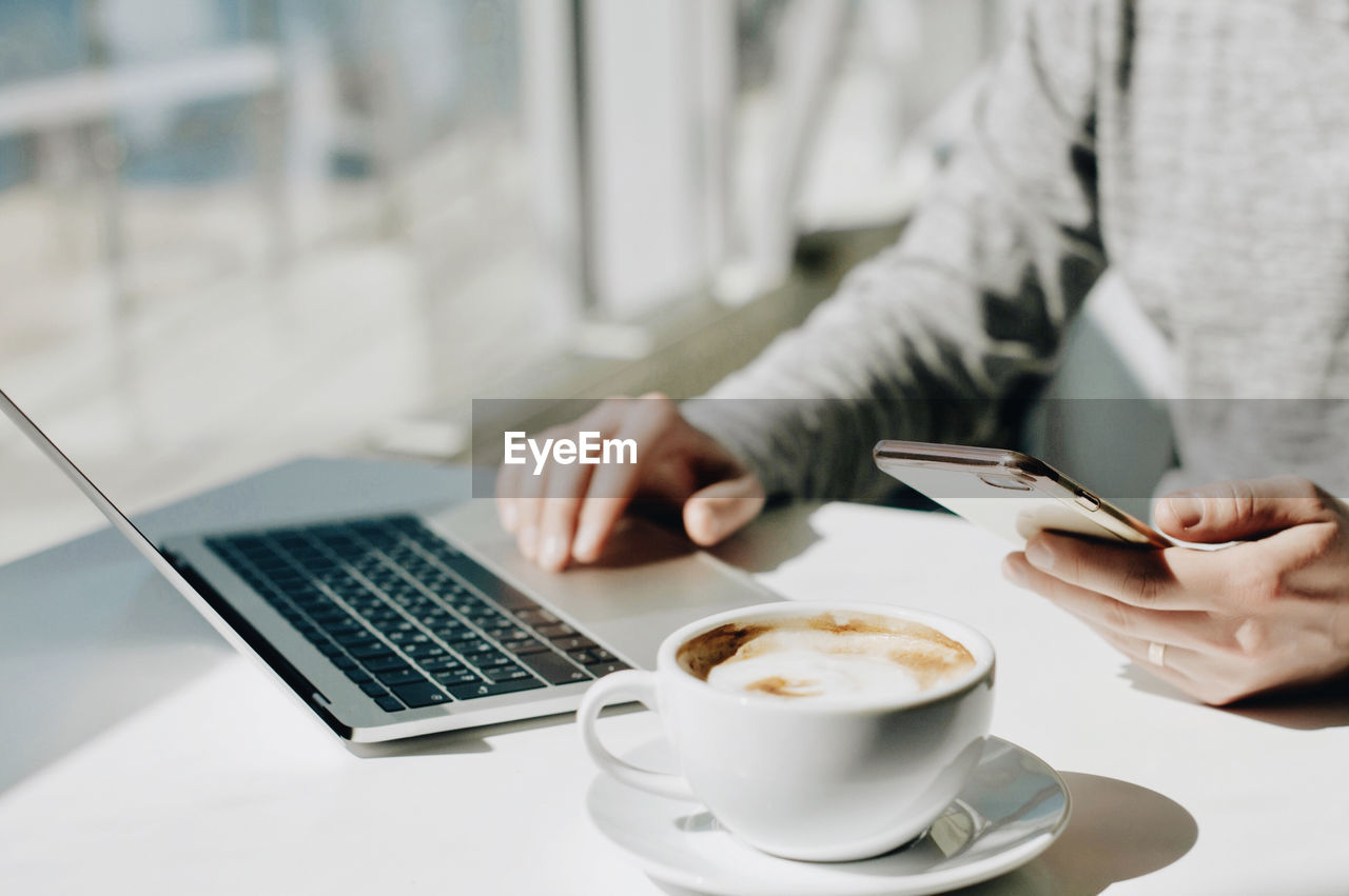 Midsection of man using laptop by coffee at table in cafe