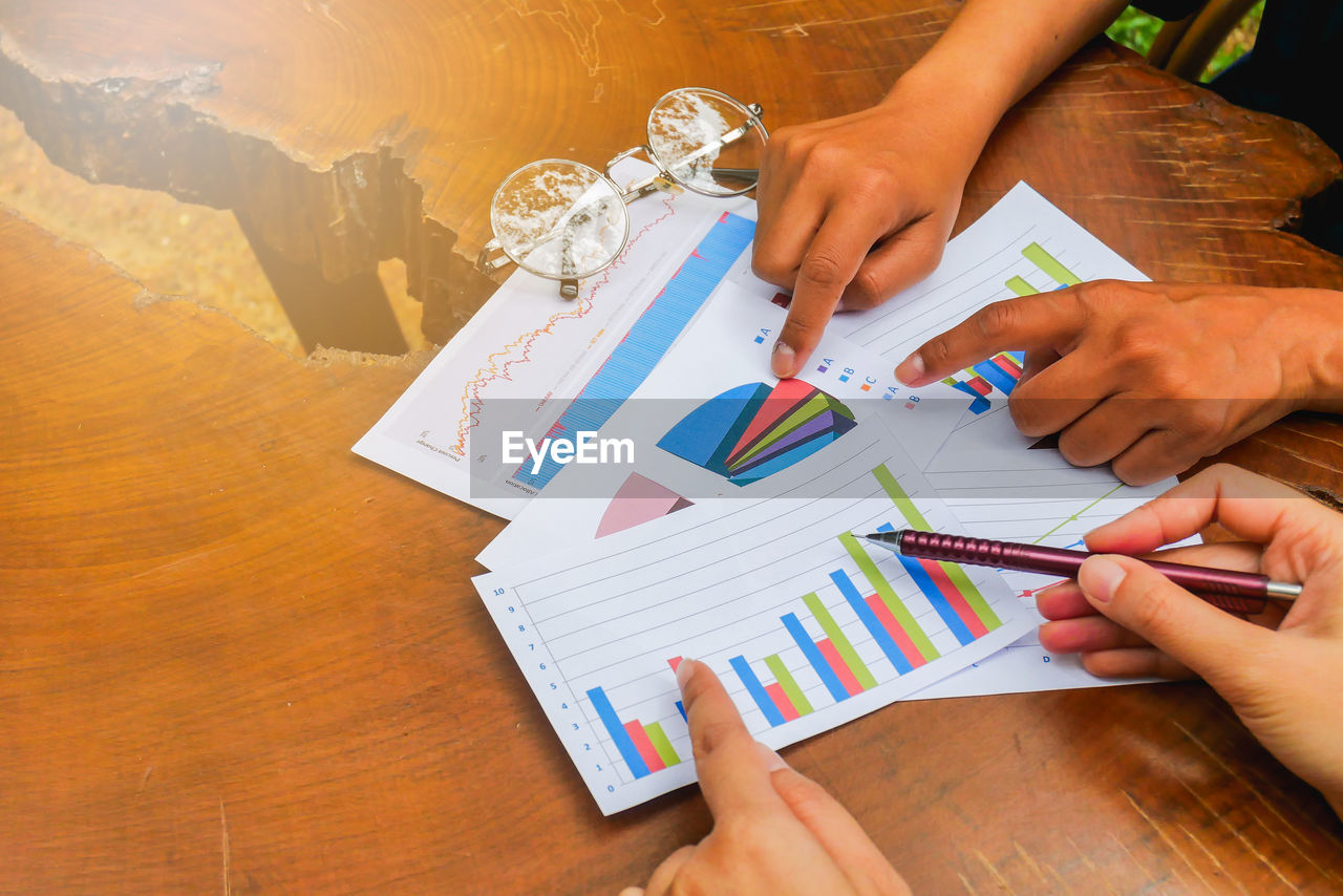 Cropped image of people discussing over graphs on table