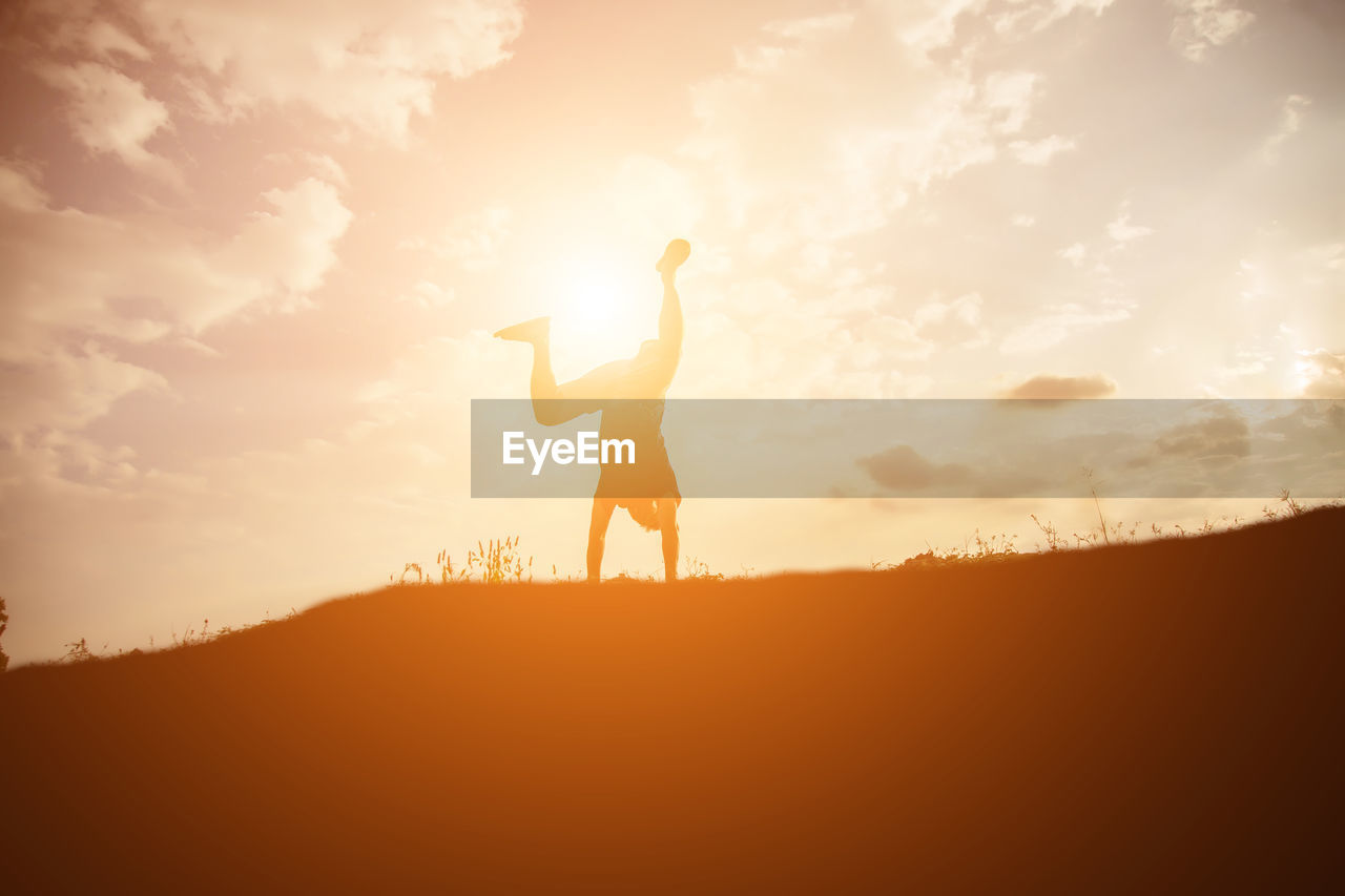 Silhouette man doing handstand on land against sky during sunset