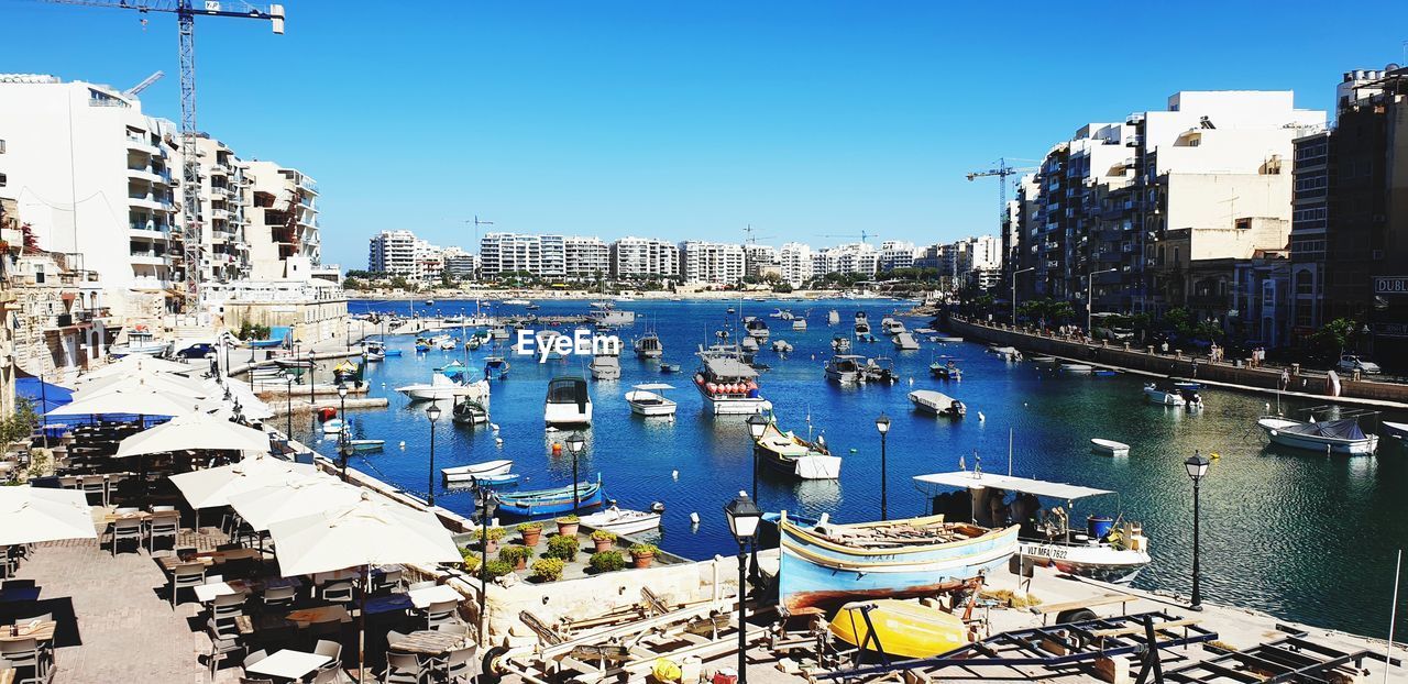 BOATS MOORED IN HARBOR AGAINST BUILDINGS