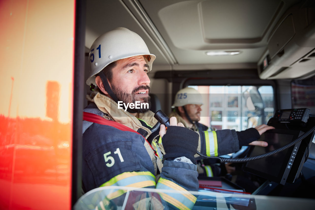 Mid adult firefighter talking on microphone while sitting with coworker in fire truck