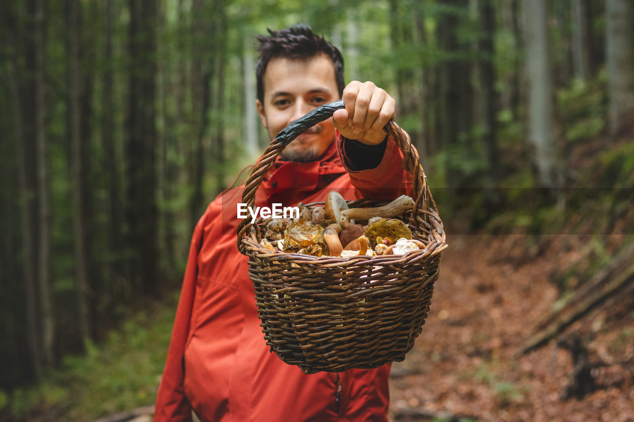 Man in outdoor clothing holds a basket full of mushrooms