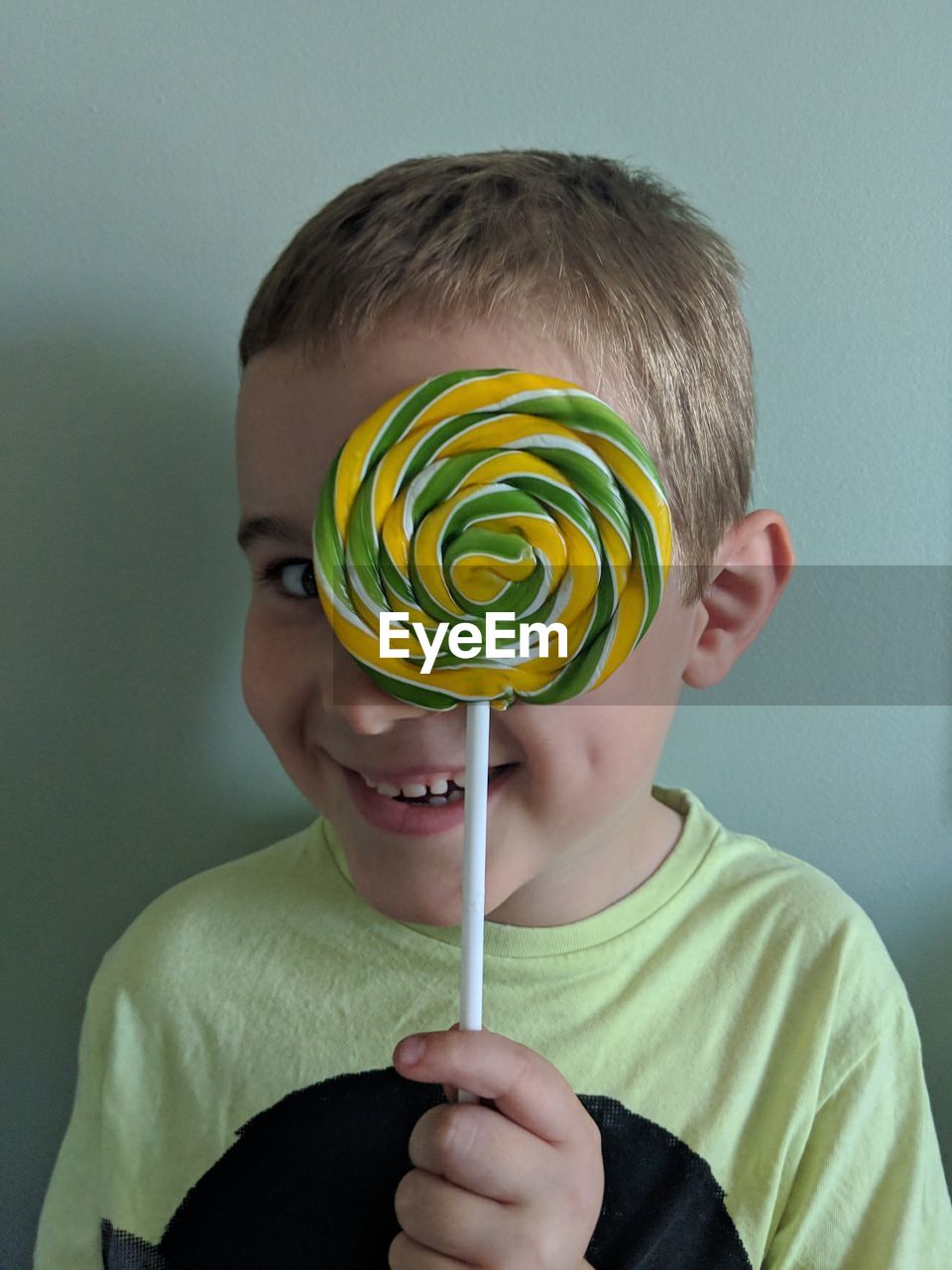 Portrait of smiling boy holding lollipop against wall