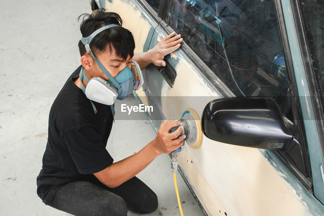 High angle view of young man working with equipment on car in garage