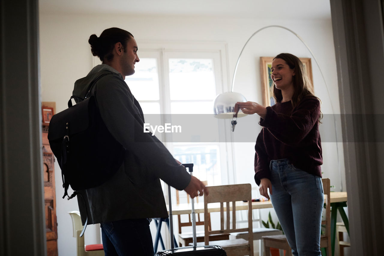 Smiling woman holding keys while talking to man in apartment on sunny day