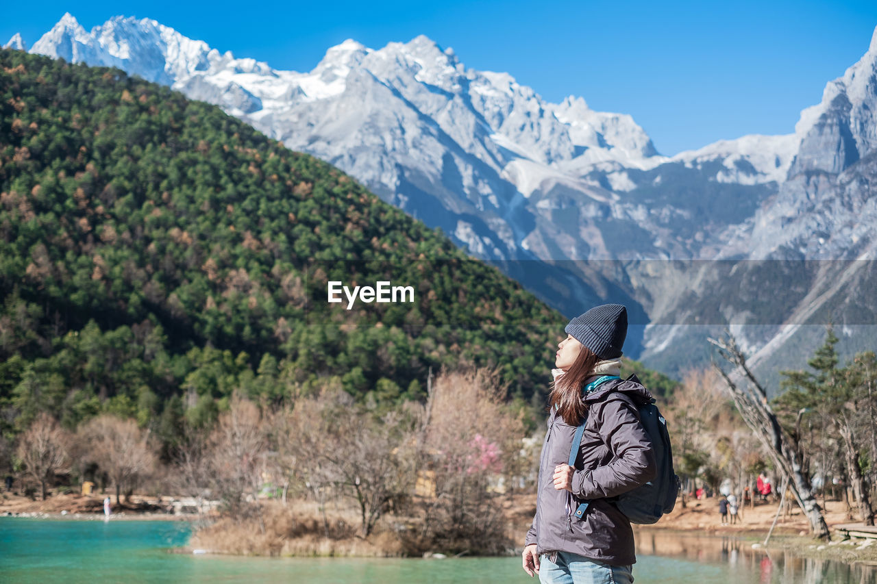 Side view of woman wearing backpack while standing against mountains during winter