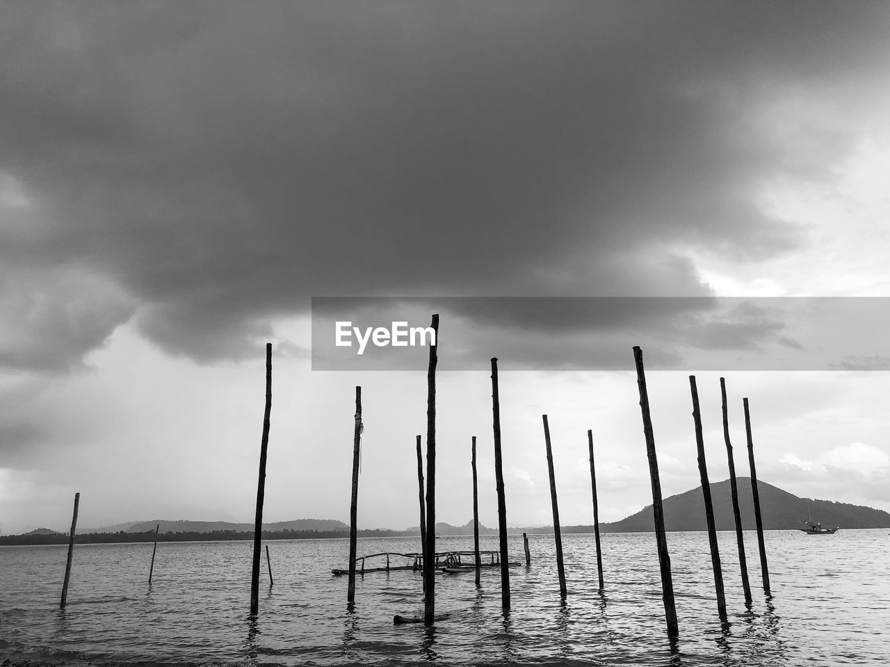 WOODEN POSTS IN SEA AGAINST CLOUDY SKY