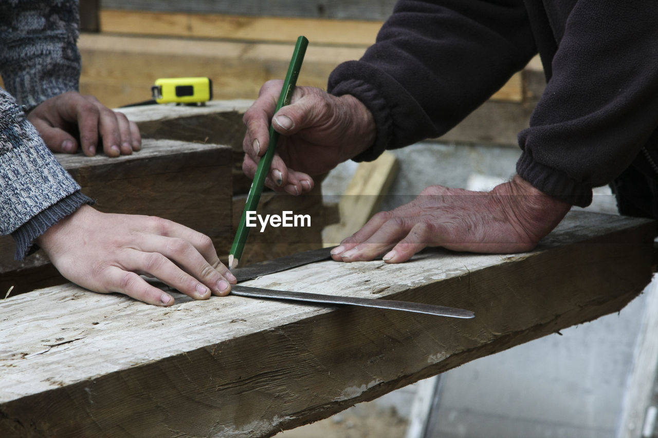 Midsection of carpenters measuring wood while working in carpentry workshop