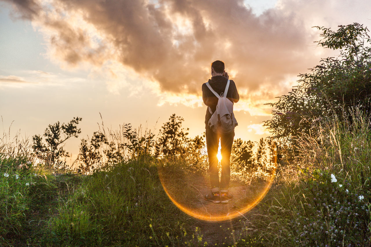 Rear view of man standing on field against sky during sunset