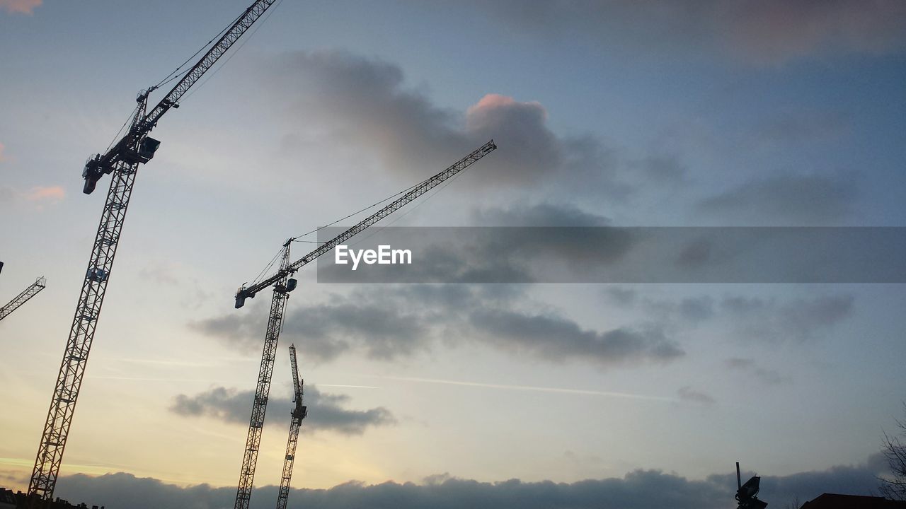 Low angle view of cranes against cloudy sky during sunset