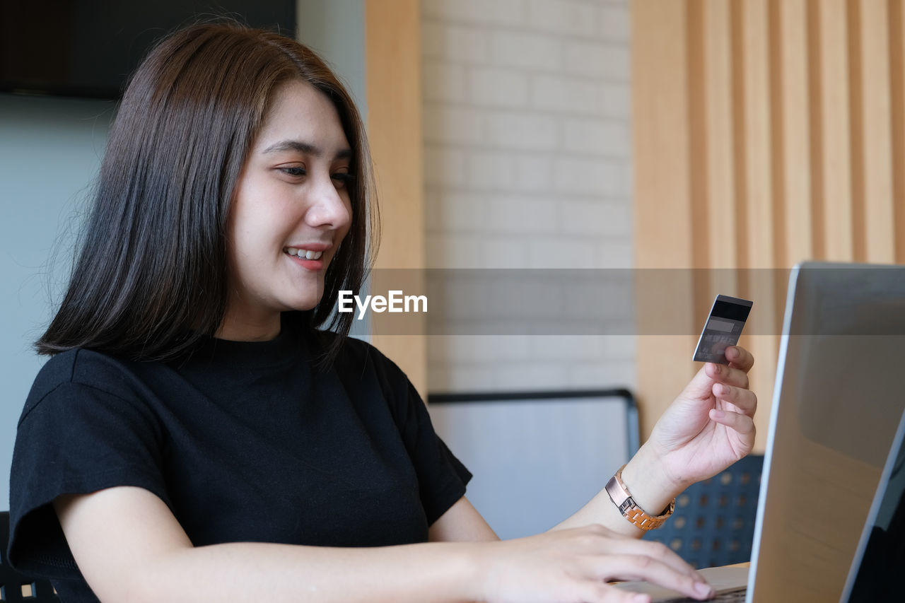 PORTRAIT OF SMILING YOUNG WOMAN USING PHONE