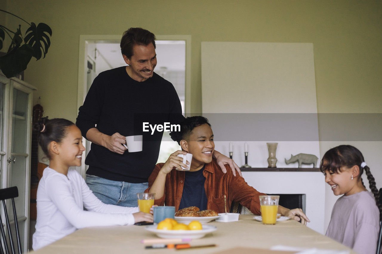 Happy gay parents enjoying breakfast with daughters while sitting at dining table in home