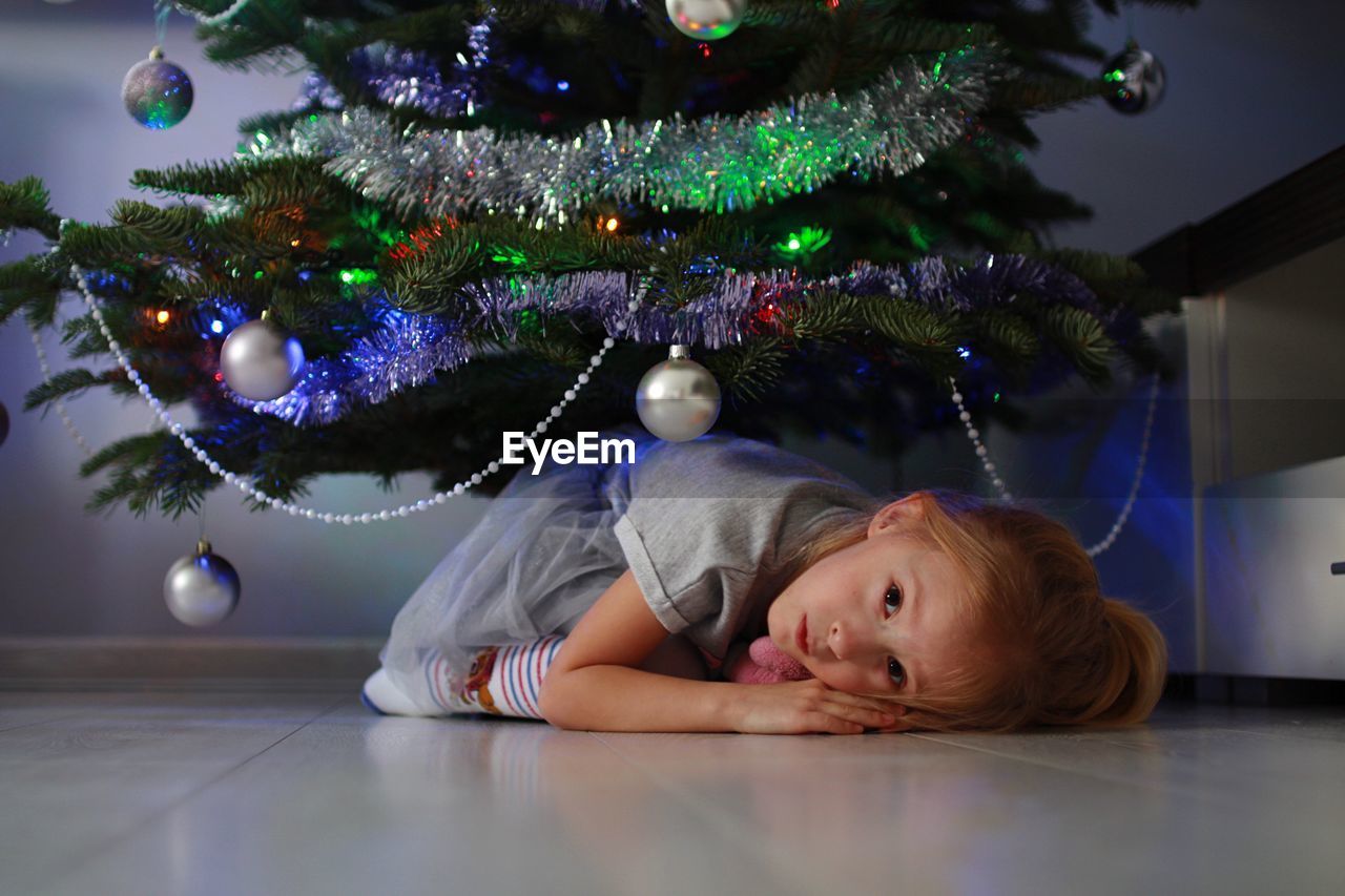 Portrait of girl lying down on floor by christmas tree