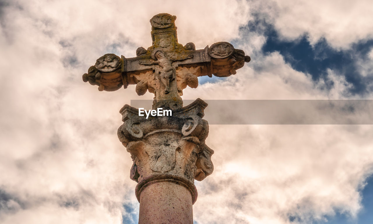 Close-up to an ancient stone cross, carved and adorned with religious motifs.