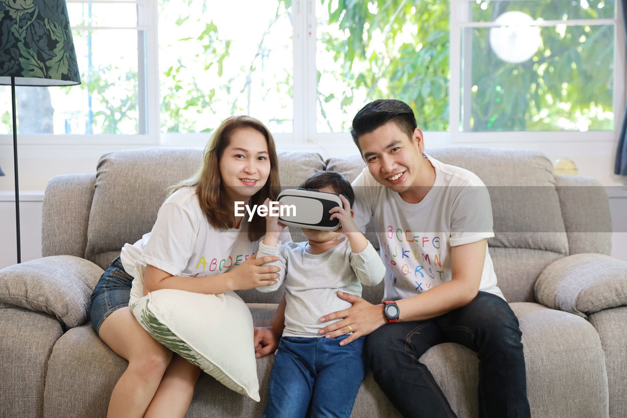YOUNG COUPLE LOOKING AT CAMERA WHILE SITTING ON SOFA AT HOME