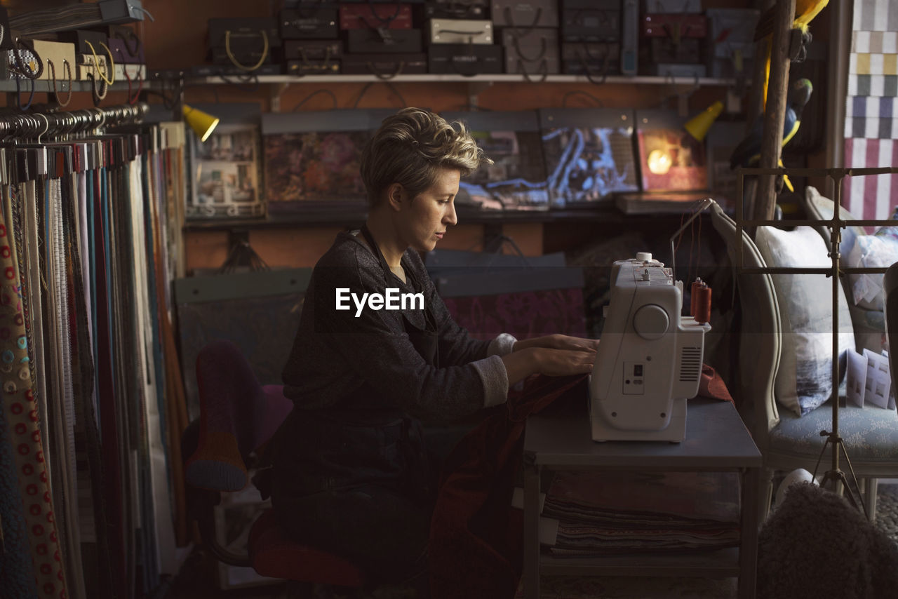 Side view of female fashion designer using sewing machine in studio