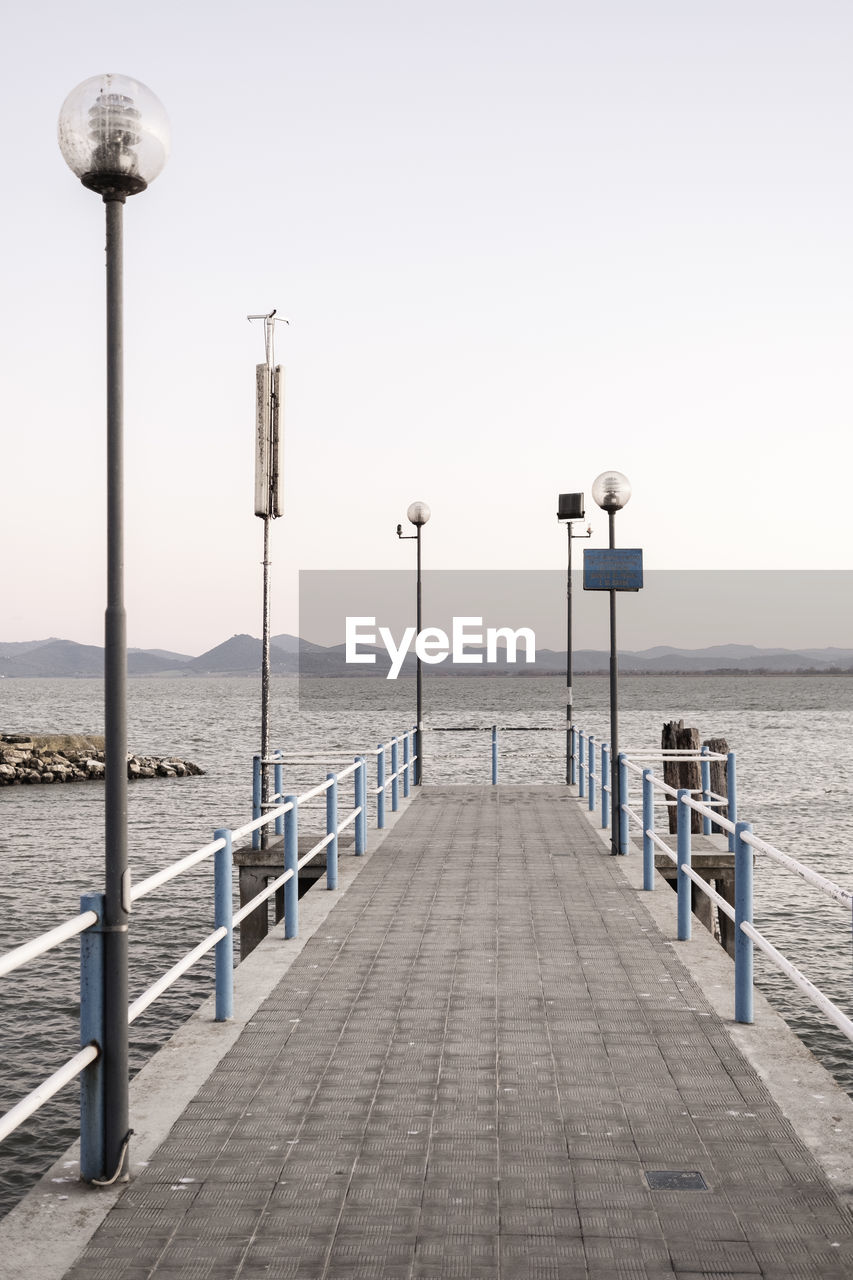 Street lights on pier by sea against clear sky