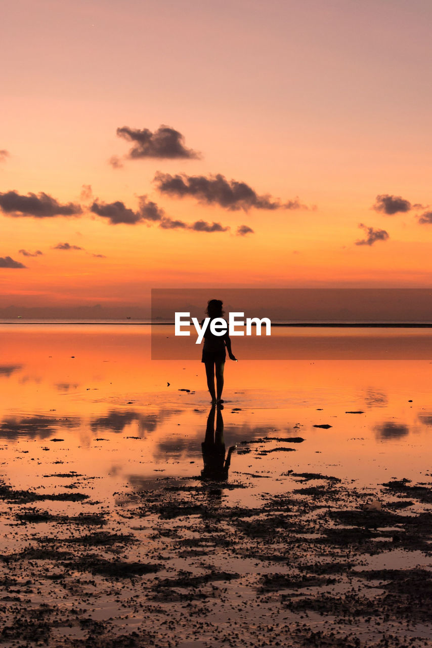 Woman walking at beach against sky during sunset