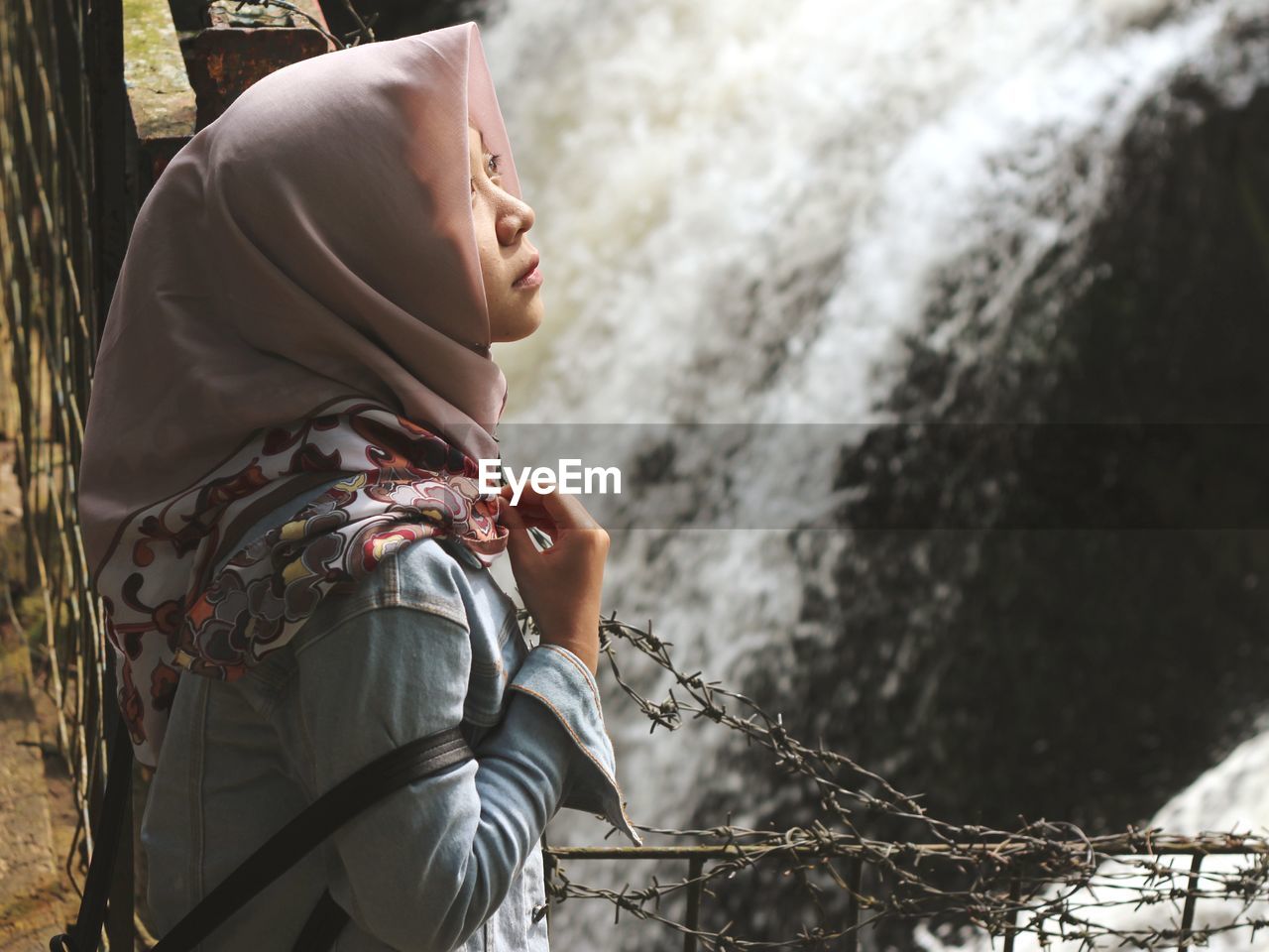 Side view of woman wearing hijab standing against waterfall