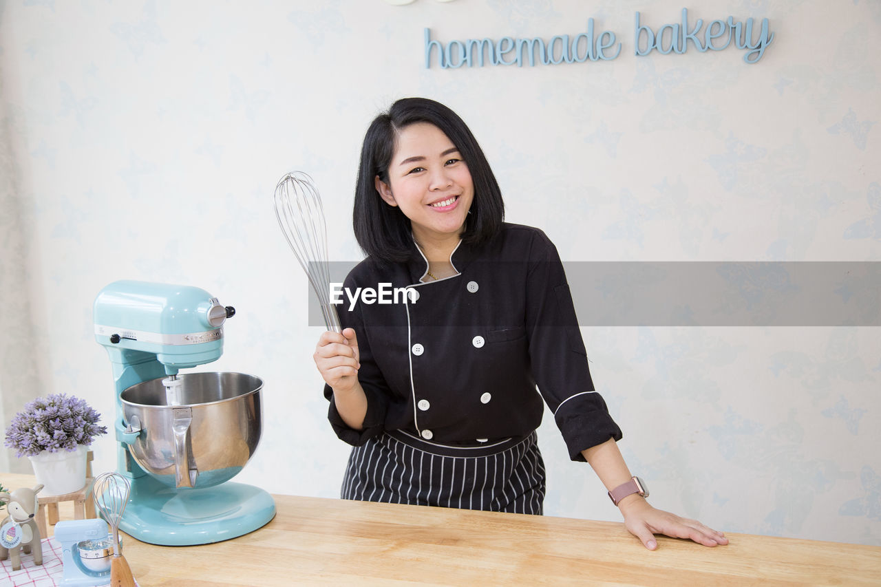 Portrait of smiling chef holding whisk while standing in kitchen