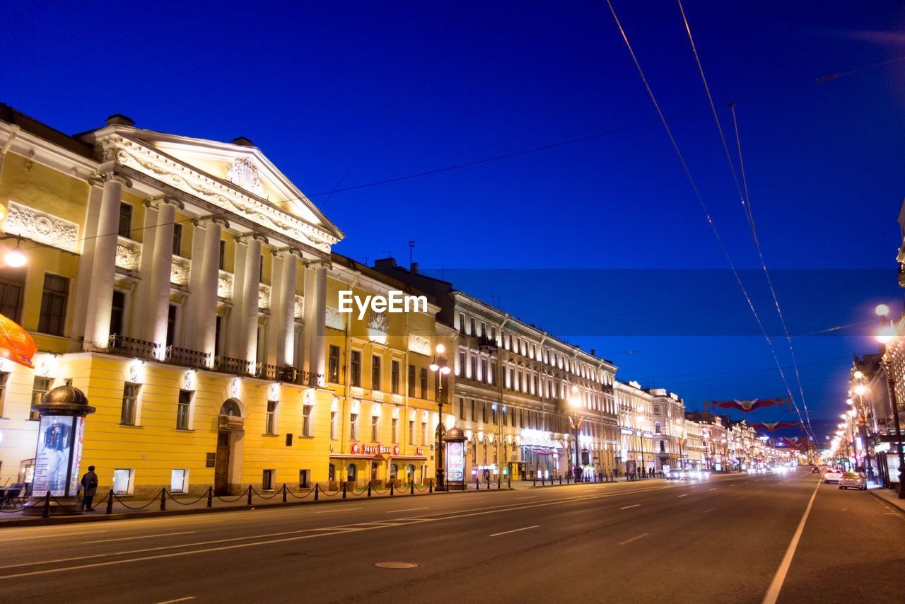 ILLUMINATED STREET AMIDST BUILDINGS AGAINST SKY