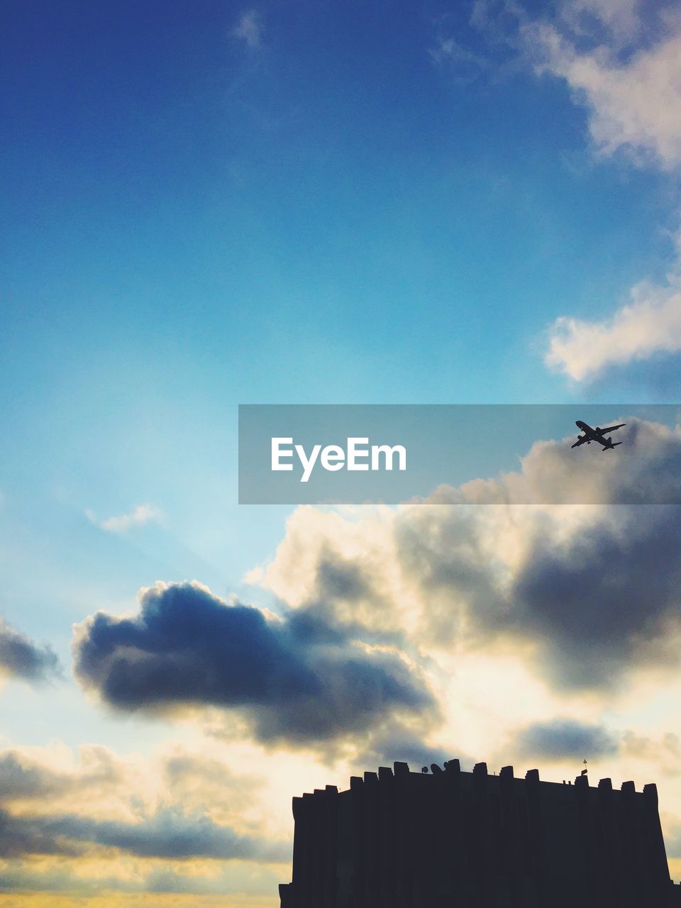 Low angle view of silhouette airplane flying over historical building against cloudy sky